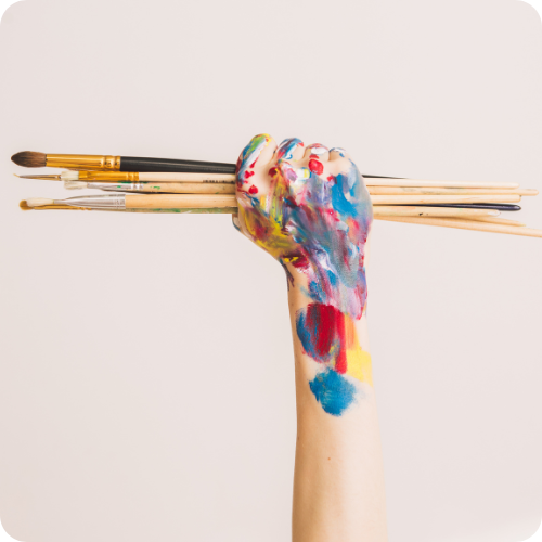 A hand holding paintbrushes triumphantly in the air, symbolising ARKK’s empowering approach to regulatory reporting.